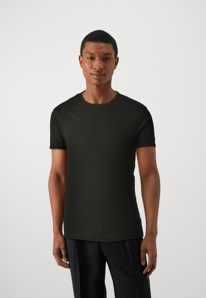 Camiseta negra de manga corta en una tela suave y elástica. Presenta un cuello redondo y un sutil detalle de logo en el pecho.