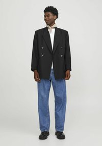 Zwarte dubbelbreasted blazer van gladde stof, met ronde revers en knopen aan de voorkant, gecombineerd met losse blauwe spijkerbroeken en zwarte schoenen.