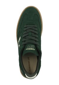 Zapatilla de ante verde con puntera redonda, parte superior texturizada, acento blanco, cordones planos y suela de goma marrón. La marca en la lengüeta dice "Flamingos Life."