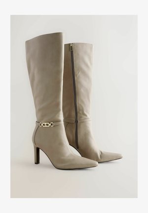 Knee-high beige leren laarzen met puntige neuzen, een zijrits en een smalle riemdetail met een gouden gesp. De hakken hebben een gematigde hoogte.