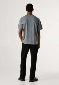 Sivé bavlnené tričko s okrúhlym výstrihom, krátkymi rukávmi a voľným strihom, doplnené čiernymi nohavicami a čiernou obuvou.