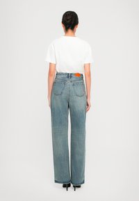 Jeans azzurri chiari a vita alta con design a gamba dritta, dotati di due tasche posteriori e di un'etichetta con logo arancione sul cinturino.