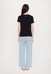 Zwarte t-shirt met korte mouwen en ronde hals, voorzien van een klein EA7-logo op de bovenrug, gecombineerd met lichtblauwe wijde jeans.