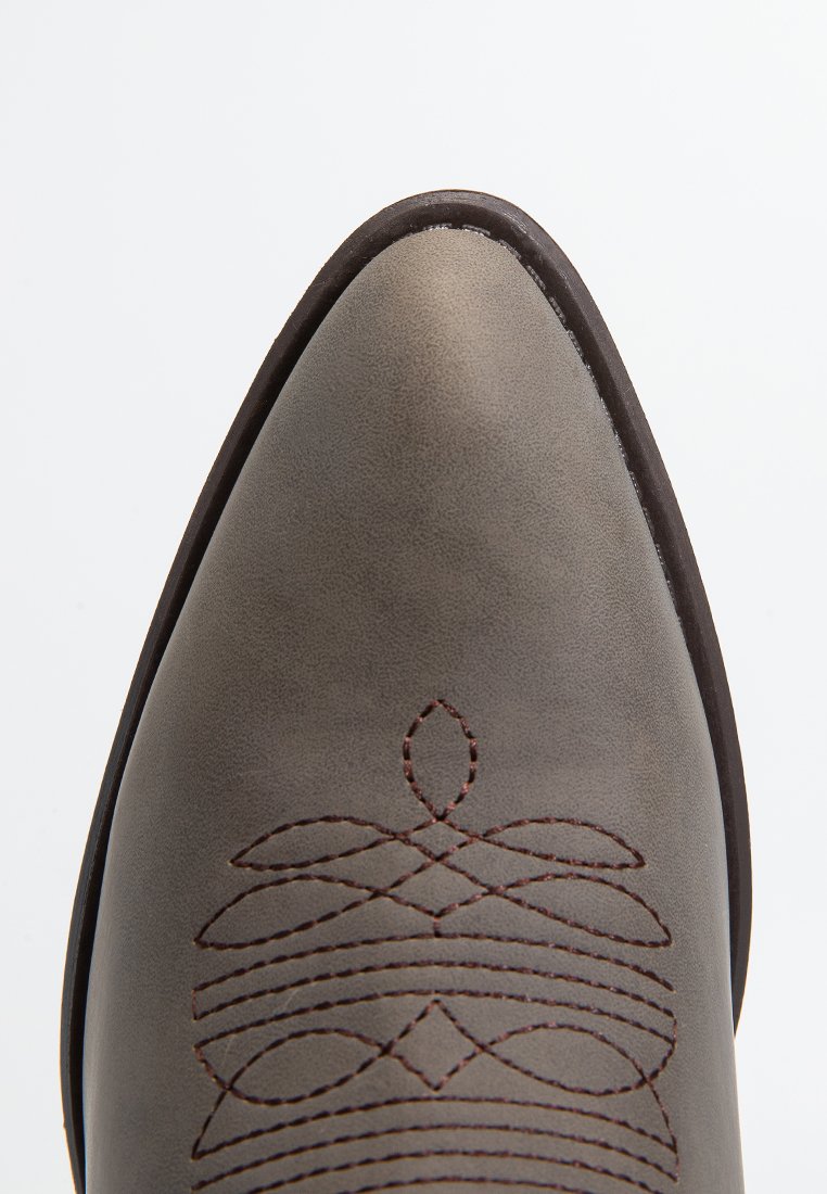 Bota de cuero gris con puntera afilada, que presenta un elegante bordado marrón en un patrón floral en la superficie superior y una textura suave.