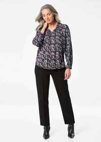 Blusa a maniche lunghe in tessuto nero con un motivo astratto colorato, abbinata a pantaloni neri a gamba dritta e stivaletti a punta.