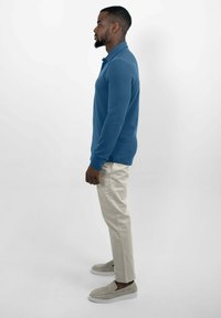 Polo met lange mouwen in effen blauwe stof, gecombineerd met beige slim-fit broeken en lichtgrijze instappers. Zijaanzicht.