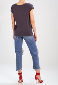 Šedý top s krátkým rukávem, volný střih, v kombinaci se světlými modrými džíny s worn efektem, se třepenými lemy, a červenými vysokými podpatky.