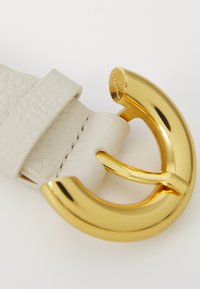 Weißer Leder-Gürtel mit strukturiertem Finish, ausgestattet mit einer großen, glänzenden goldenen Rundschnalle mit modernem Design und aufwendigen Details.