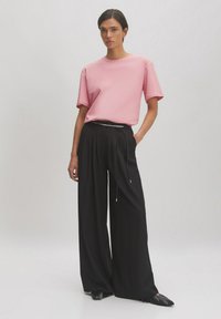 Rosa Kurzarm-T-Shirt kombiniert mit schwarzen weiten Hosen, die über einen Kordelzug verfügen. Glattes Material mit lockerer Passform.