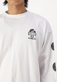 White long-sleeve shirt featuring a black graphic of a character holding a record. Graphics on the chest and both sleeves. Cotton material.