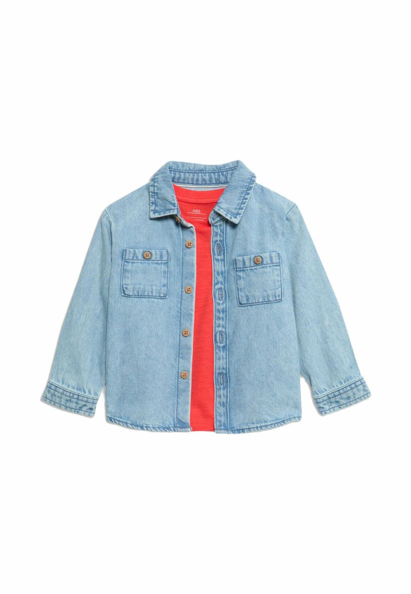 Giacca di jeans azzurro chiaro con maniche lunghe, chiusura con bottoni, due tasche sul petto e bottoni marroni. Indossata sopra una maglietta rossa.