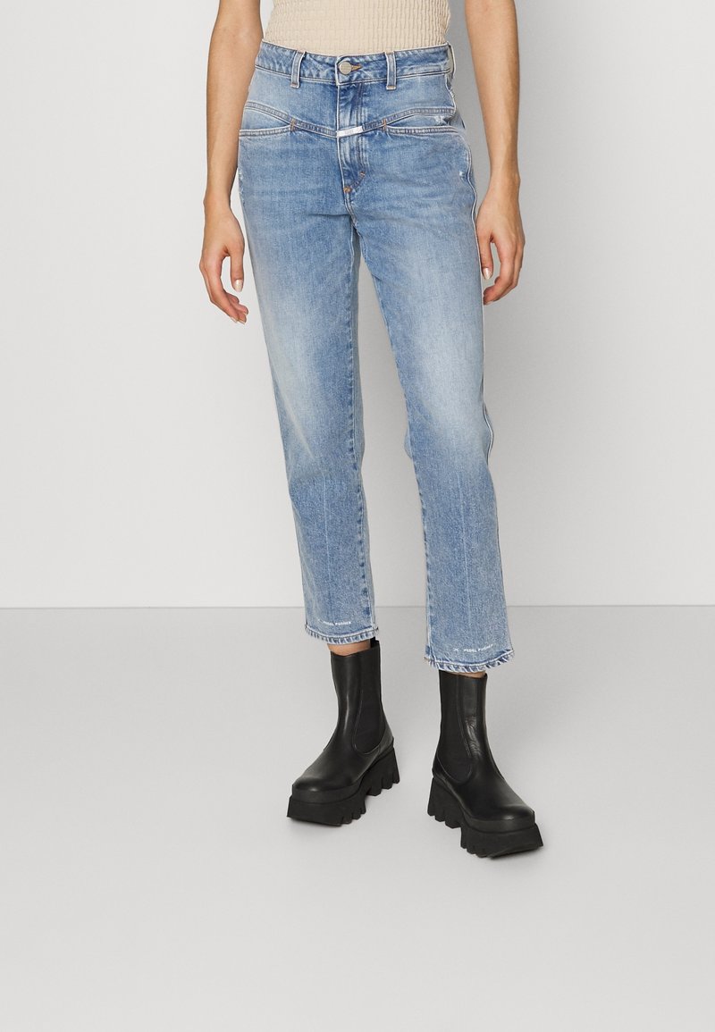 Femme portant un jean droit taille haute bleu clair avec une ceinture double unique et des bottes noires à plateforme épaisses.