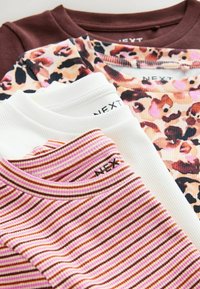 Quattro t-shirt impilati: una marrone, una bianca, una con stampa leopardata e una a righe rosa, bordeaux e crema. Tutte hanno una texture a costine.