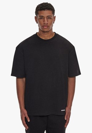 T-shirt noir à manches courtes en coton, avec un col rond et une petite étiquette au bas. Coupe ample avec une texture lisse.