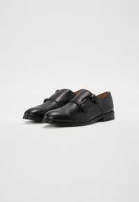Black leather shoes with a rounded toe, double buckle accents, and a smooth texture. Low heel and minimalistic design.