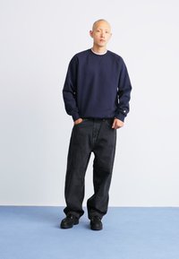 Navy sweatshirt with ribbed neckline, paired with black loose-fitting jeans and dark sneakers, against a light background.