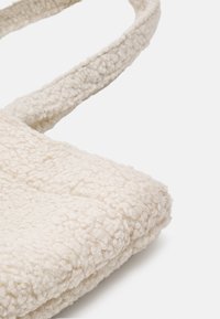 Beige textured tote bag with soft, fluffy fabric, featuring two sturdy straps and a rectangular shape. Suitable for everyday use.