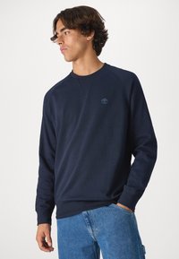 Sudadera azul marino con mangas largas, cuello redondo, puños acanalados y un pequeño logo en el pecho. Tejido suave con una textura lisa.