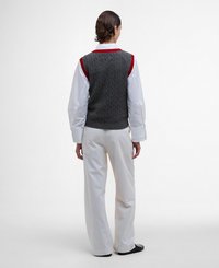 Gilet en tricot gris avec motif en relief, bordé de rouge, superposé sur une chemise blanche à boutons et associé à un pantalon blanc ample.