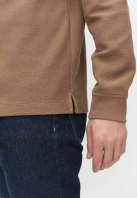 Bruine textuur lange mouwen blouse met een geribd patroon en zijslitsen, gecombineerd met donkerblauwe denim. Zachte stof met aansluitende manchetten.
