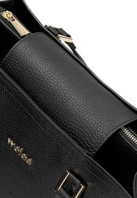 Zwarte leren handtas met een gestructureerde afwerking, voorzien van een gouden rits, metalen accenten en een klep-sluiting ontwerp.