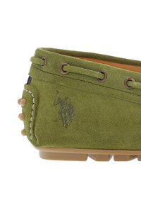 Grön mockaskor med låg profil, detaljerad sömnad, metallöglor och en texturerad gummisula. Har ett embossat logotyp på sidan.