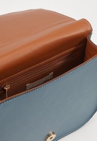 Blue leather handbag with a brown leather interior, featuring a zippered pocket and gold hardware accents. Smooth texture, structured design.