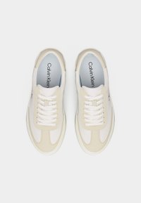 Paire de baskets Calvin Klein blanches et beiges avec lacets, vues de dessus sur un fond blanc uni.