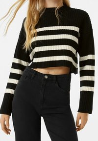 Czarnobiały, paskowany, krótkie sweter o prążkowanej fakturze, zestawiony z czarnymi, wysokim stanem dżinsami z zapięciem na guziki z przodu.