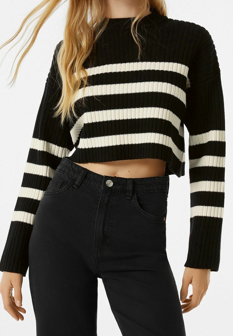 Czarnobiały, paskowany, krótkie sweter o prążkowanej fakturze, zestawiony z czarnymi, wysokim stanem dżinsami z zapięciem na guziki z przodu.
