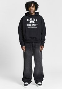 Must mustaga, millel on kiri "ATELIER RETERNITY 2018 LOOVJUHT". Kombineeritud laia tumehallide teksadega ja mustade sandaalidega, millel on valged aktsendid.