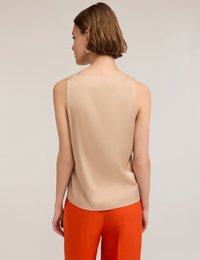 Top sin mangas beige con textura suave y escote redondeado, combinado con pantalones naranjas vibrantes. La vista trasera resalta un diseño minimalista.