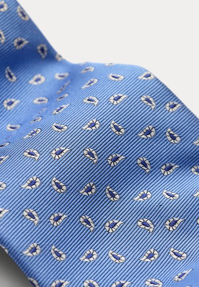 Γαλάζια μεταξωτή γραβάτα με επαναλαμβανόμενο μικρό σκούρο μπλε και λευκό παϊνέλ μοτίβο σε ύφασμα με ριγέ υφή.