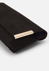 Černá semišová kabelka se zlatým metalovým akcentem. Vyniká hladkou texturou a obdélníkovým tvarem, navržena pro nošení v ruce.