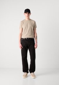 Μπέζ κοντομάνικο μπλουζάκι, μαύρο τζιν, μαύρη ζώνη, ανοιχτόχρωμα αθλητικά παπούτσια και μαύρο καπέλο. Απλή σχεδίαση με ελάχιστες λεπτομέρειες.