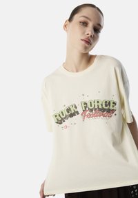 T-shirt in cotone color crema con maniche corte, caratterizzato da una stampa grafica di "ROCK FORCE Festival" in verde e rosso con effetti invecchiati.