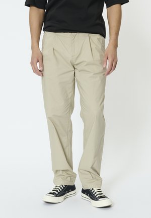 Beżowe, lekkie spodnie o luźnym kroju i plisowanym przodzie. Połączone z czarnymi niskimi trampkami z białymi sznurowadłami i gumowymi podeszwami.