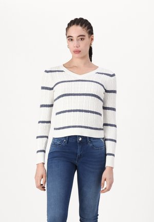 White cable-knit sweater with blue horizontal stripes, V-neckline, and long sleeves, paired with blue denim jeans.