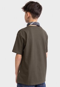 Olivegrünes Baumwoll-T-Shirt mit kurzen Ärmeln, lockerer Passform und einer dezent strukturierten Oberfläche. Getragen mit einem schwarz-grau gemusterten Bandana.