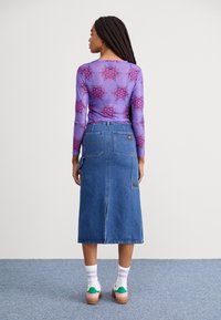 Haut à manches longues violet avec motif floral rose, associé à une jupe midi en jean bleu avec poches arrière et fente sur le côté.