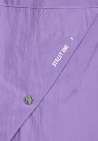 Lilla stofskjorte med en let tekstureret overflade, en sølvknap og trykt "STREET ONE" logo langs sømmen.