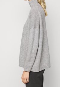 Grå strikket rullekrave-trøje med løs pasform, ribstrikkede manchetter og kant. Fremstillet af blødt materiale med sømløs skulderdesign.