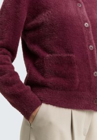 Bordeaux, fluffy cardigan met een ronde hals, knoopsluiting en een voorzak. Heeft een zachte textuur en een geribde zoom.
