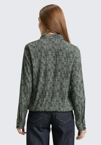 Langärmliges Hemd mit grünen und schwarzen vertikalen Streifen, mit kragenähnlichem Ausschnitt und strukturiertem Stoff. Kombiniert mit dunklen Jeans.