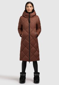 Brūns kvilts garais mētelis ar augstu apkakli un rāvējslēdzēju. Tam ir sānu kabatas un to var kombinēt ar melniem potīšu zābakiem un pielāgotiem biksēm.