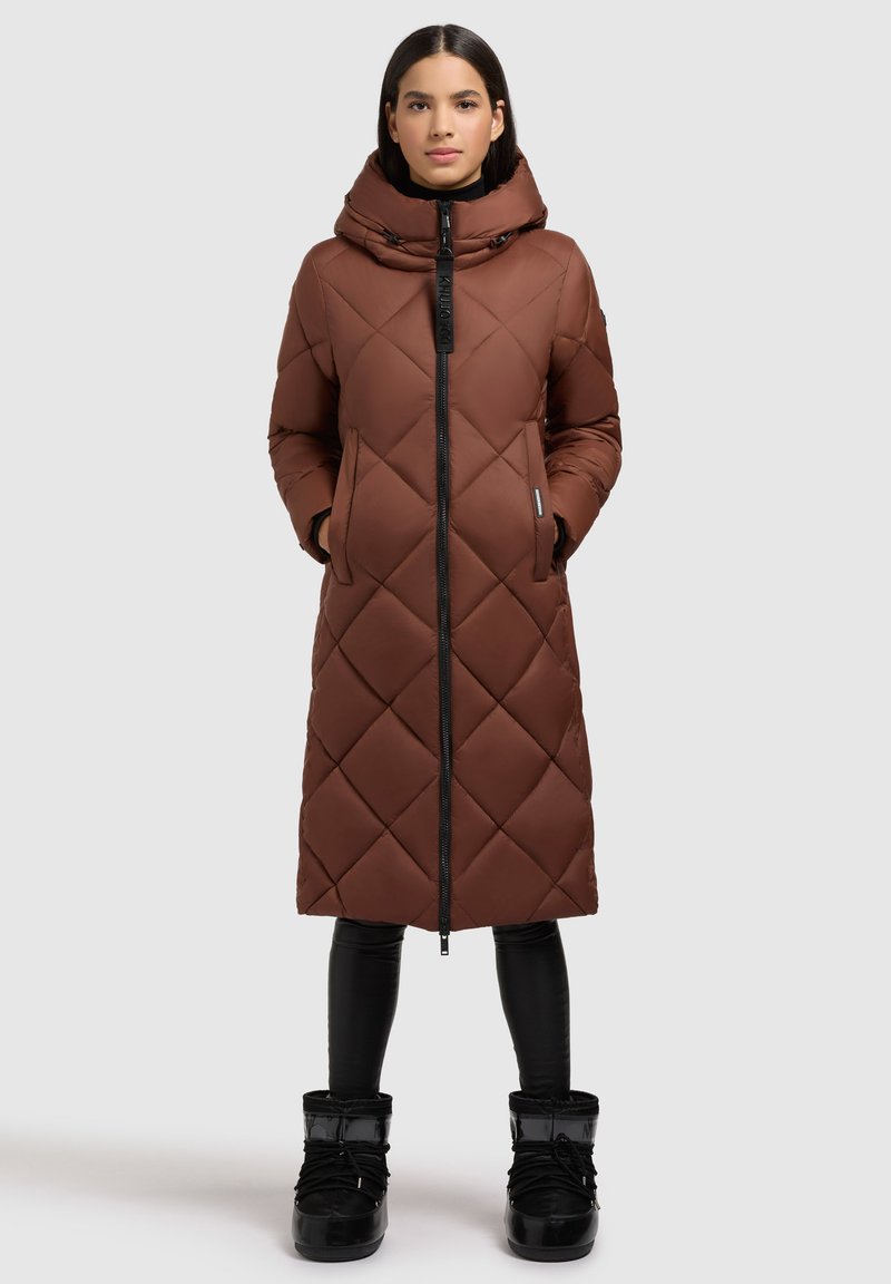 Brūns kvilts garais mētelis ar augstu apkakli un rāvējslēdzēju. Tam ir sānu kabatas un to var kombinēt ar melniem potīšu zābakiem un pielāgotiem biksēm.