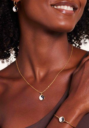 Ensemble de bijoux en ton doré comprenant un collier avec pendentif yin-yang et des boucles d'oreilles assorties, avec des détails en émail noir et blanc. Formes simples et circulaires.