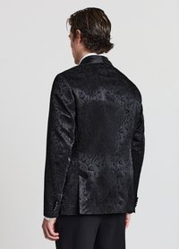 Giacca da completo in broccato nero con motivo floreale testurizzato, chiusura con un solo bottone e rever a punta. Finitura effetto seta, vestibilità su misura.