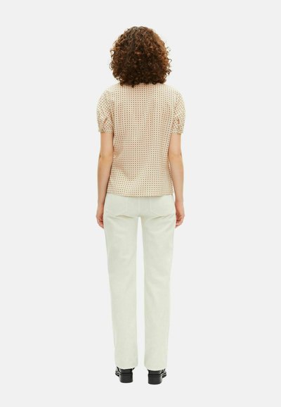 Crème blouse met polka dots en korte mouwen, met een ronde halslijn, gecombineerd met witte rechte broek en zwarte schoenen, gezien van achteren.
