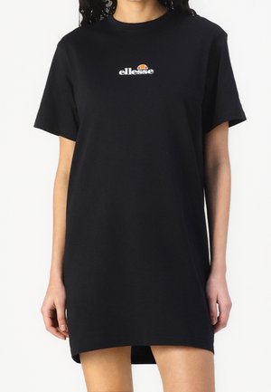 Kobieta w czarnej sukience typu T-shirt z krótkim rękawem, z małym białym i pomarańczowym logo „ellesse” na środku klatki piersiowej.